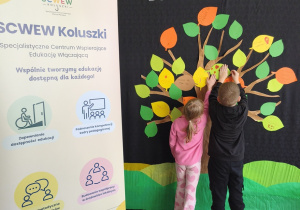 Dzieci przywieszają swoje listki na drzewie, nad drzewem napis "Każdy ma coś do zaoferowania"