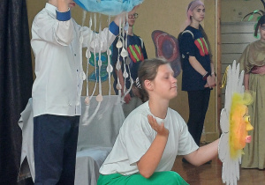 Chłopiec stoi trzymając chmurkę, dziewczynka kucając trzyma Słońce