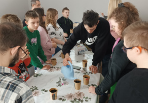 Uczniowie podlewają zasiane w doniczkach rośliny.